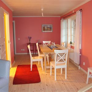 Rosa rum med röd matta och matbord med vita stolar framför ett fönster med vita gardiner. 