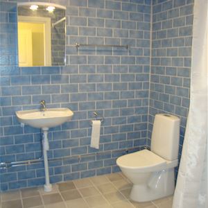 Wc och handfat i badrum med blått kakel och naturfärgat klinkers. 