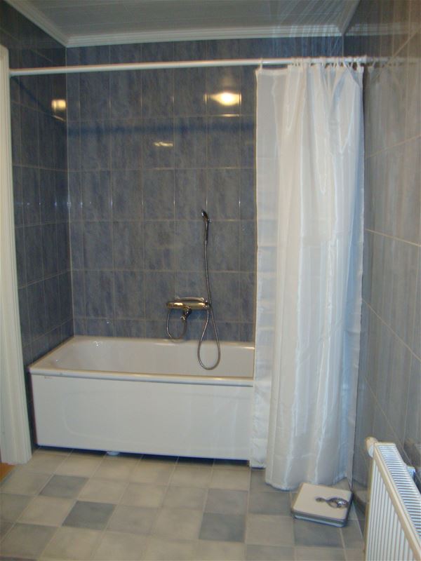 Badkar med vitt duschdraperi i badrum med blått kakel och naturfärgat klinkers. 