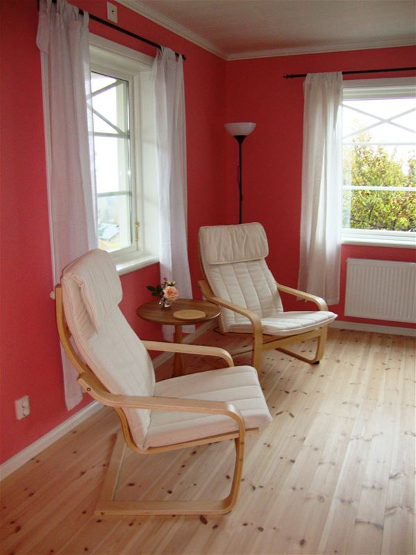 Two white armchairs in a room with red walls and wooden floor. 