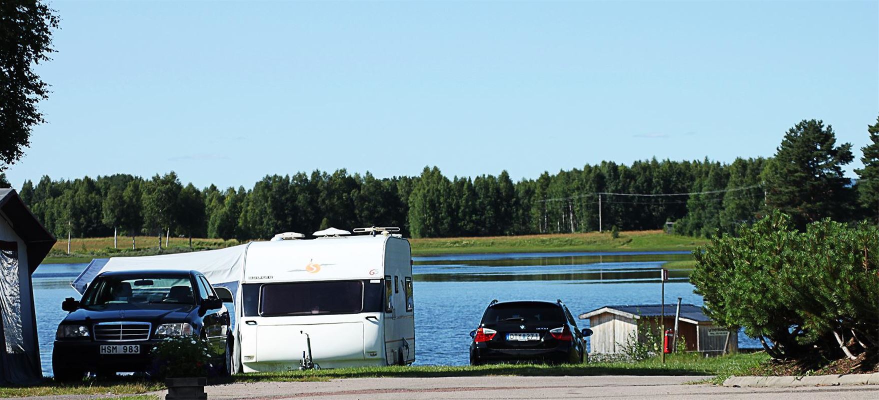 Cars and a caravan with the river in the background.