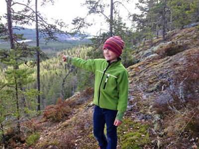 A boy in a green shirt pointing out to forest, lakes and mountains.