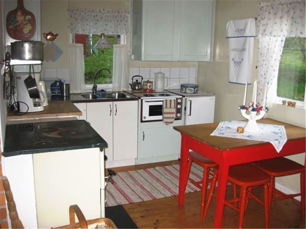 The kitchen with a wooden stove and an electric stove, a kitchen table with four stools.