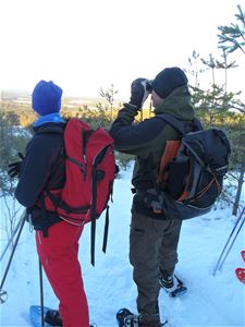 Two people with backpacks look out over the expanses. Snowshoes on their feet.