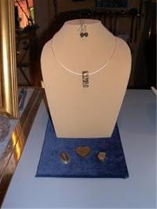 A bust with a jewelry in a silver chain. In front of the bust on a blue plate are three stones.