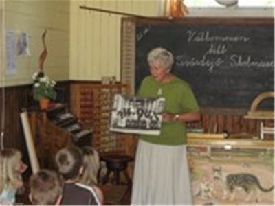 Children watching a woman in green sweater holding a black and white photo.