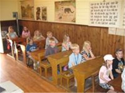 Barn sitter i äldre skolbänkar.