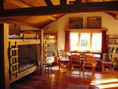 Room with wooden floor and ceiling, wooden bunkbeds and dining furniture. 