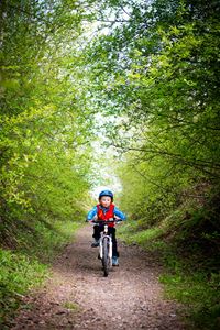 En pojke på cykel som cyklar på grusväg omgiven av grönskande träd.