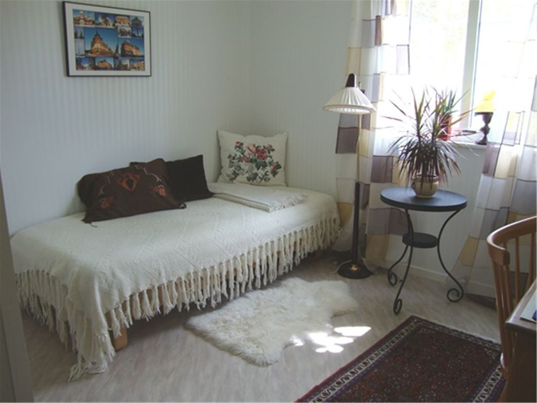 Single bed with white bedspread with lashes and a small black table with a flower on. 