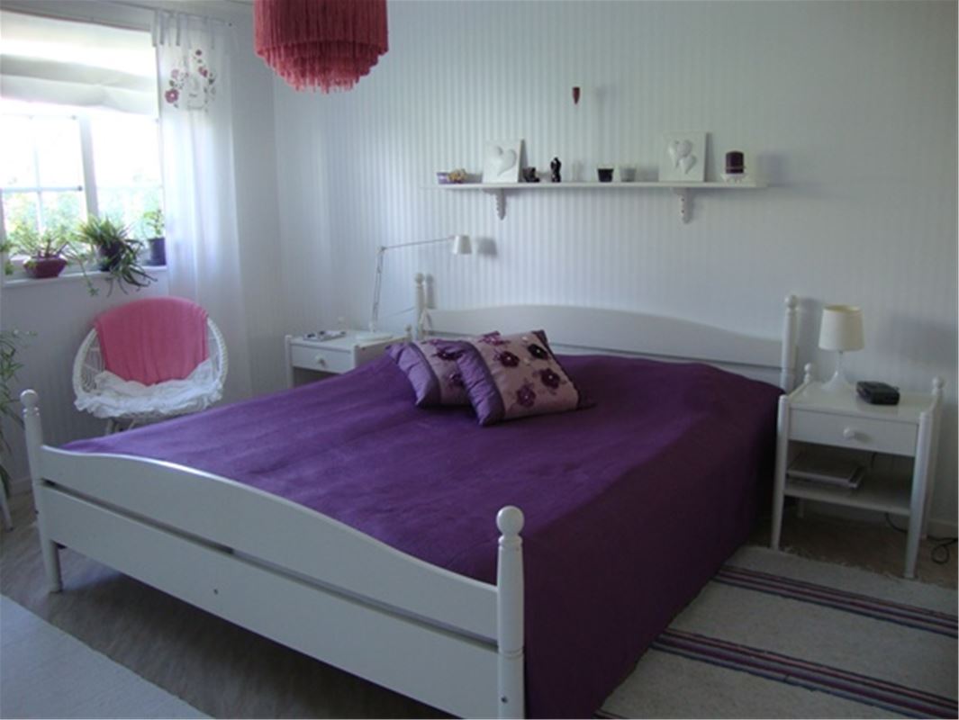 Double bed in a white bed frame and a purple bedspread. 