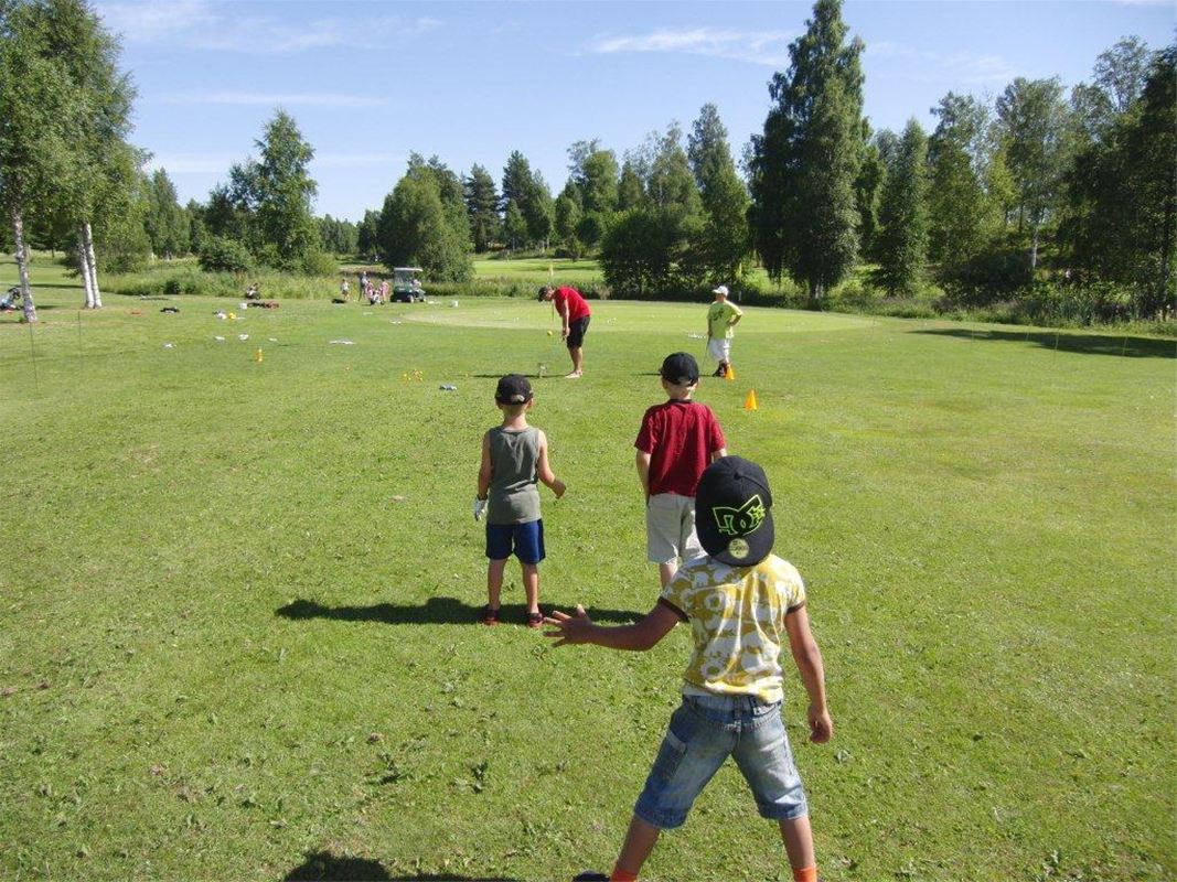 Barn står på golfbanan tillsammans med en tränare.