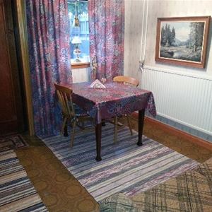 Matbord med två stolar framför ett fönster med lila, mönstrad gardin med matchande vaxduk. 