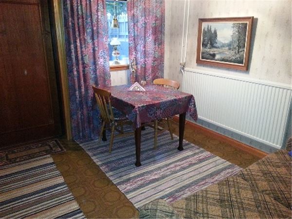 Matbord med två stolar framför ett fönster med lila, mönstrad gardin med matchande vaxduk.  