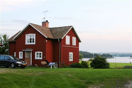 Rödmålat bostadshus med vatten i bakgrunden.