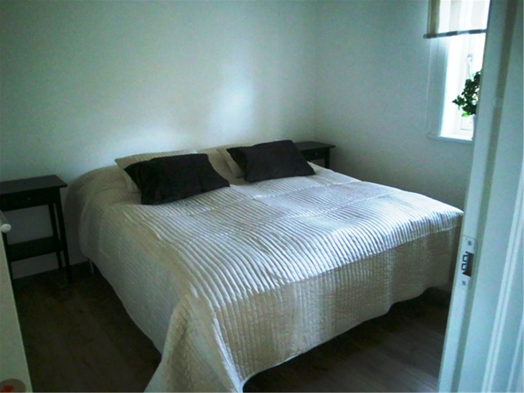 Double bed with white bedspread in a bright room. 