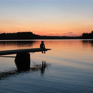 Solnedgång vid sjö med siluett av barn på brygga. 