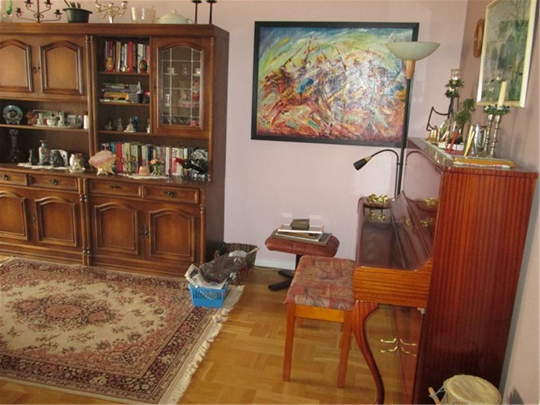 Vardagsrum med brun bokhylla, piano och en mönstrad matta på golvet. 