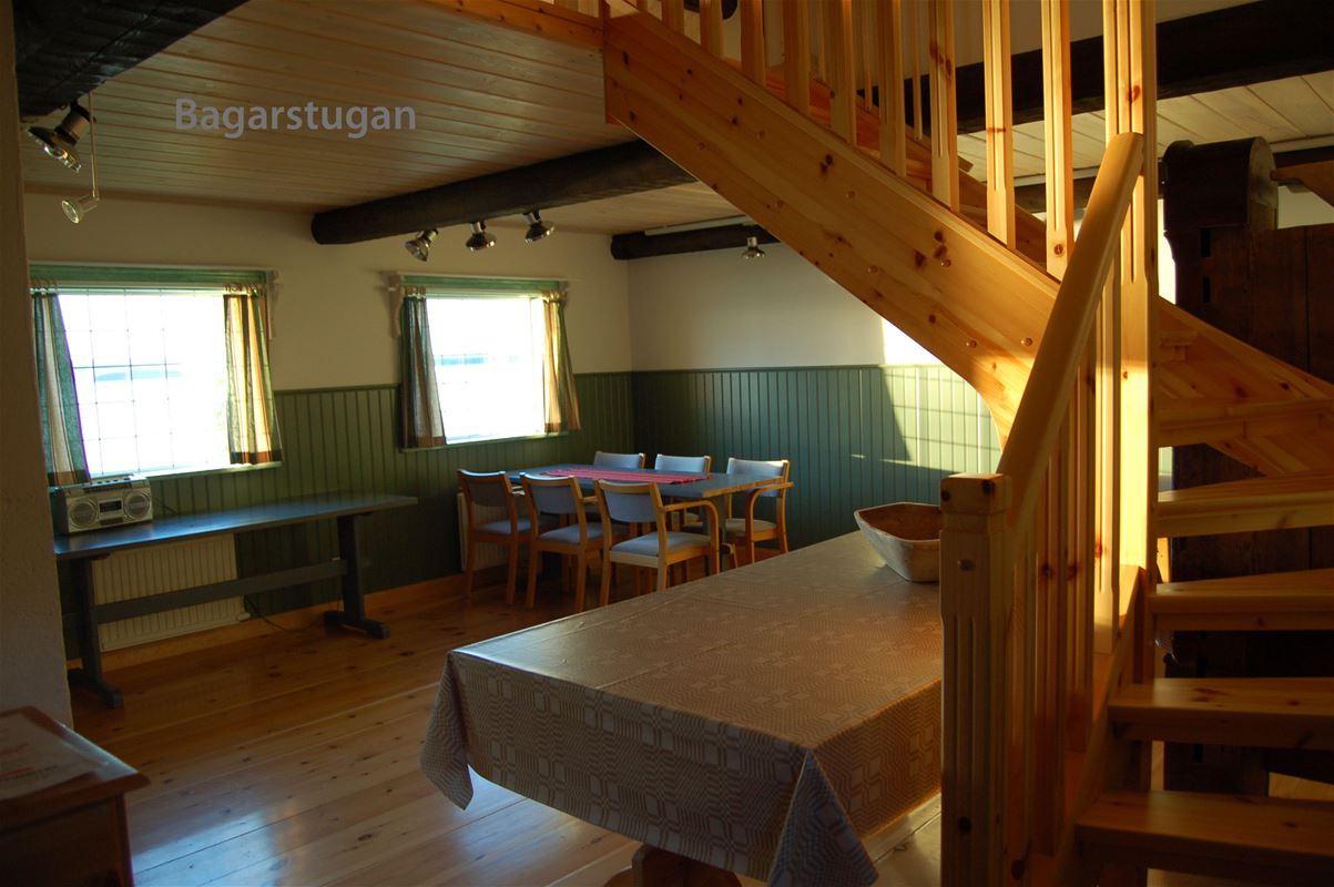 Allrum med grön bröstpanel, bord, stolar och en furutrapp till loftet.