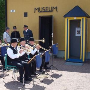 Three men playing trumpet, a yellow wall with the text museum.