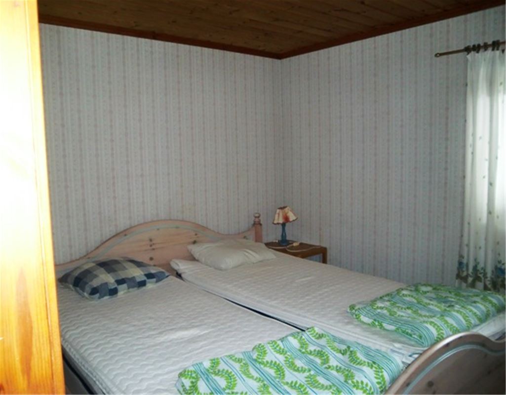 Double bed with bedframe  in a room with bright wallpaper. 