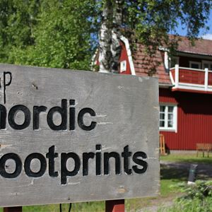 Nordic Footprints,  © Nordic Footprints, Skylt med camp nordic footprints med ett rödmålat hus i bakgrunden.
