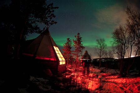 Nordlyset danser over campen mens person ser på