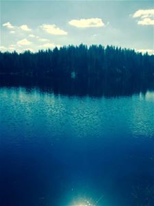 Blåskimrande sjö med skog i bakgrunden.