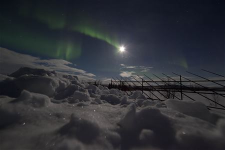 Nordlys over snø, måneskinn i bakgrunnen