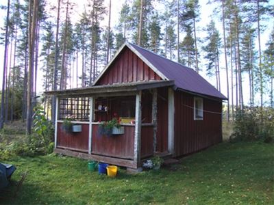 Exterior av liten rödmålad stuga med veranda.