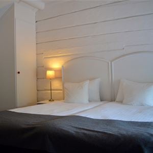 Double bed with white headboard against a white painted wooden wall.