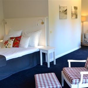 Ett rum med en säng med vit sänggavel och en rödrutig fåtölj.
