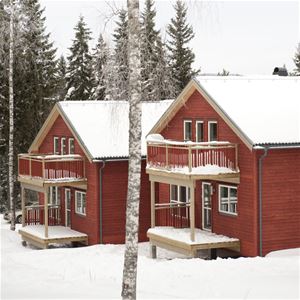 Two red log cabins surrounded by snow.