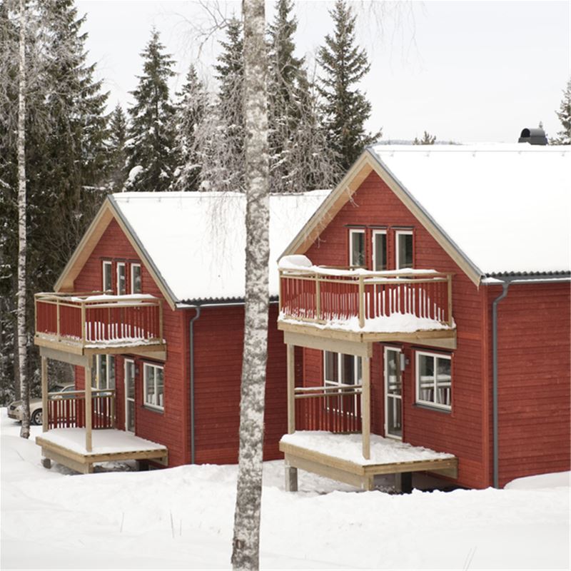 Röda tvåvåningsstugor med snö runt husen.