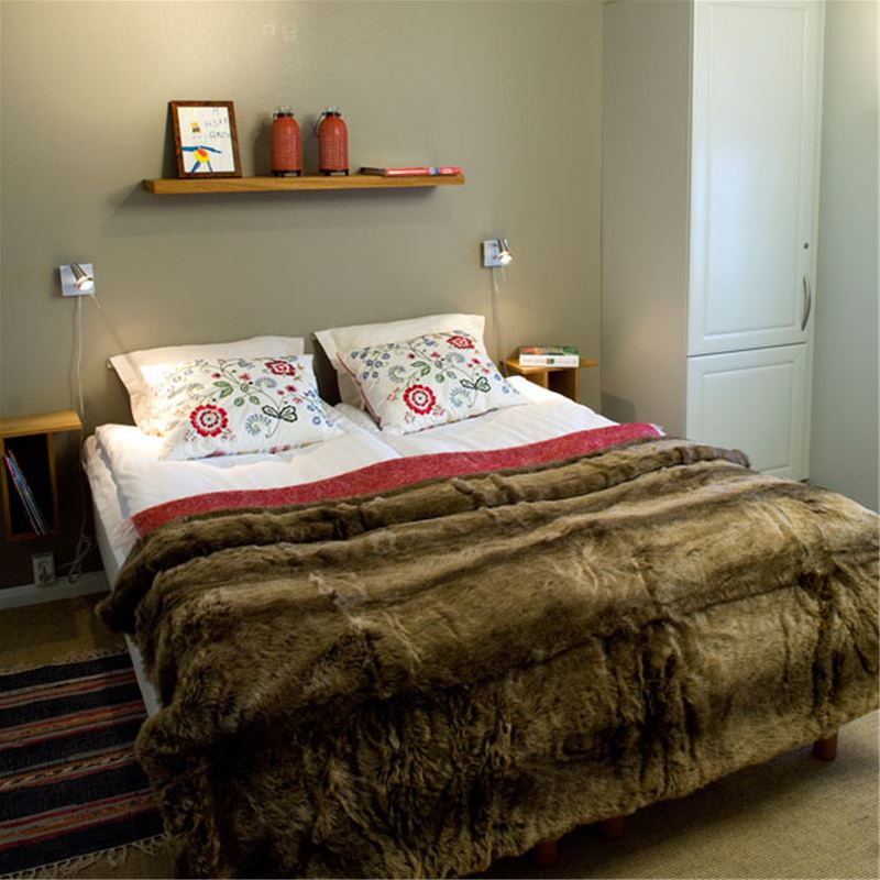 Bedrom with a doublebed, emboided cushions and a bedspread in fur.