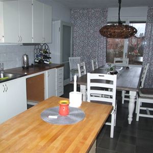 Kitchen with white cupboards and dining table with white chairs by the window. 