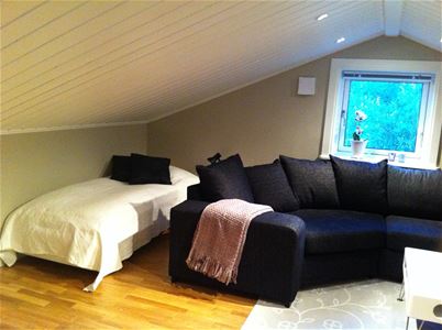 Single bed behind a large sofa under a sloping roof. 
