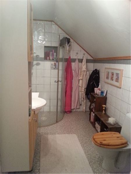 Badrum med duschväggar, kommod och toalett under snedtak.  