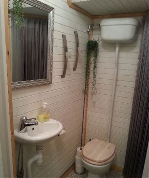 Toalett och handfat med en spegel i silverram ovanför på en vitmålad vägg av liggande panel.  