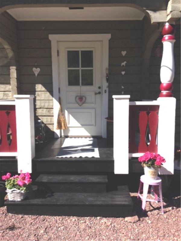 Entrén med vit dörr, svart trätrapp och ett par rosa blommor på var sida om ingången. 