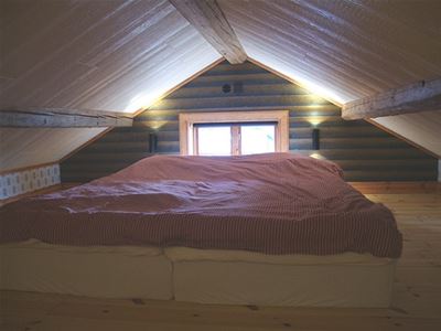 Loft with two mattresses on the floor in front of a small window. 