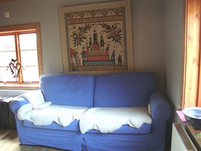 A blue sofa with white sheepskin in the sofa and a dalecarlian painting above the sofa.