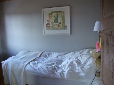 Single bed with white sheets placed to a bright wall with a small painting. 