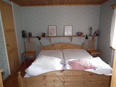 Double bed in a wooden bed frame in a small room with pattered wallpaper.