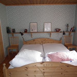 Dubbelsäng i sängram av furu i ett litet rum med mönstrad tapet. 