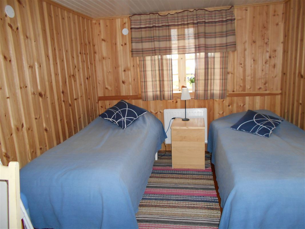 Two single beds with blue bedspread in a room with pine walls.