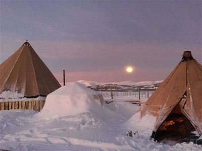 Two traditional tents in a snowy landscape with the moon and mountains in the background.
