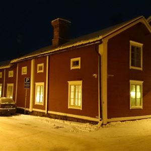 Vinterbild utifrån mot huset ii mörker med lampor som lyser i fönstren.