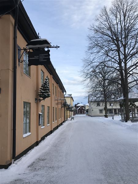 Exteriörbild vinter, hus i två våningar med gul putsad fasad, bild tagen från gatan. 