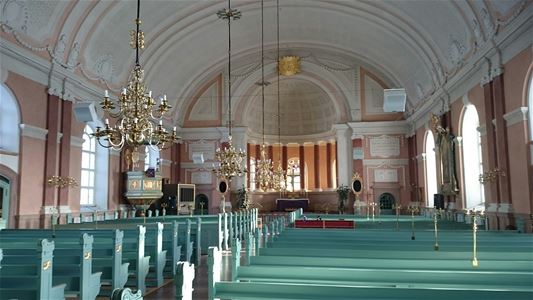 Inne i kyrkan med kyrkbänkar, ljuskronor och altare.